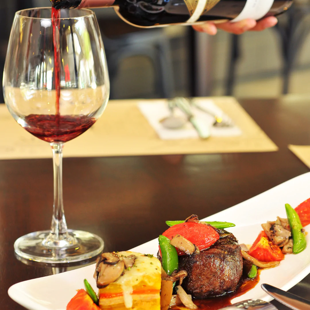 Red wine being poured next to plated steak dish.