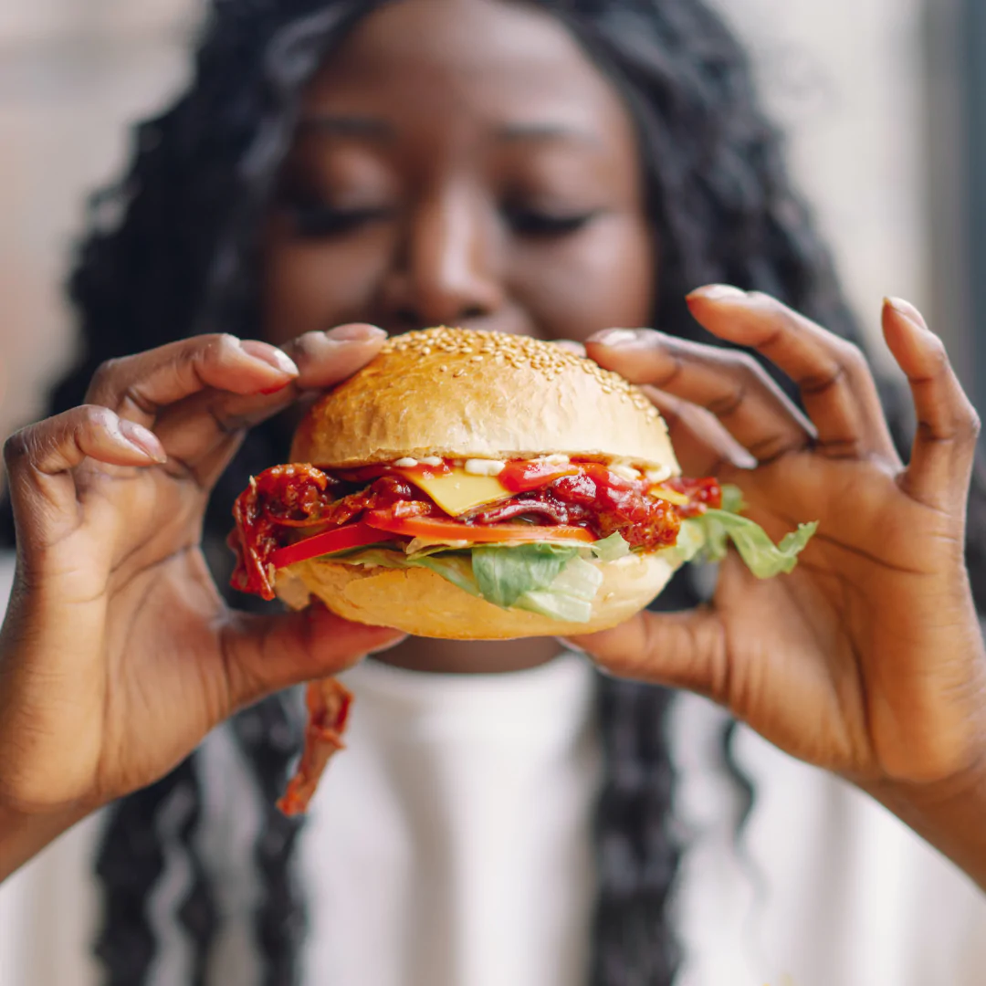 Woman holding a fresh burger with lettuce and cheese.