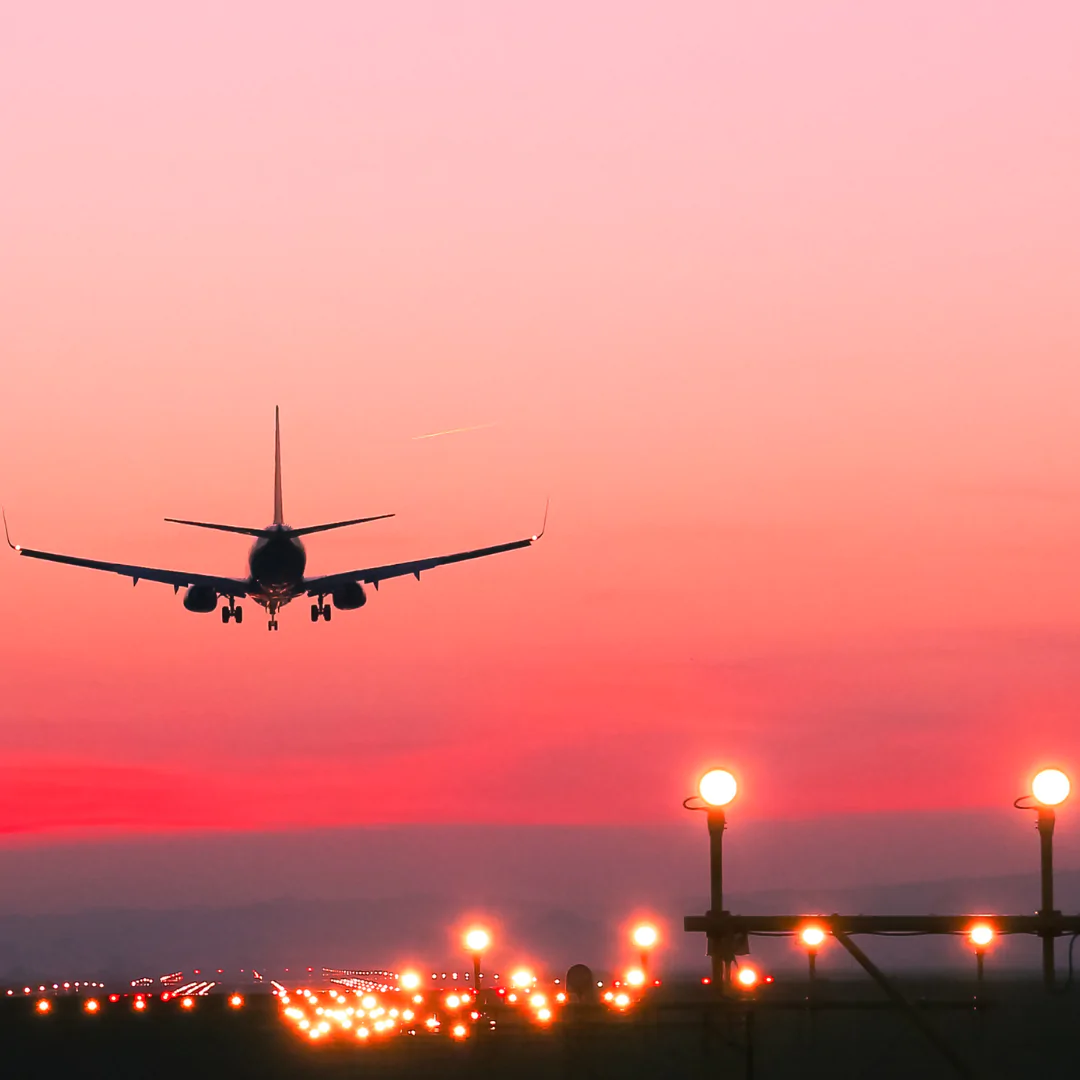 Airplane landing at sunset over illuminated runway.