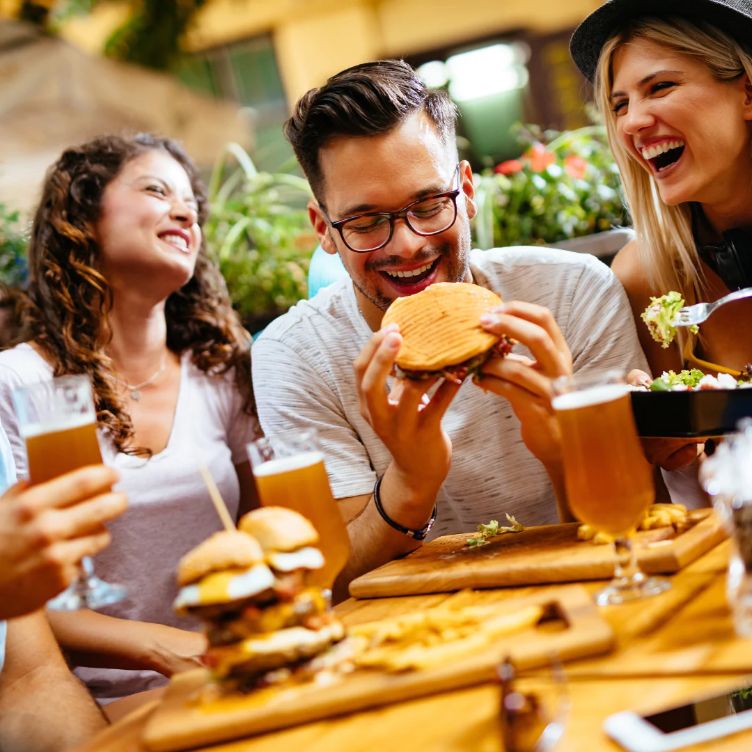 Friends enjoying burgers and beer at outdoor restaurant.