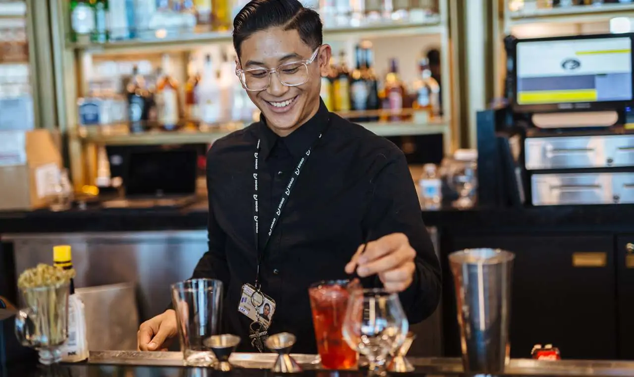 Bartender preparing a red cocktail behind the bar.