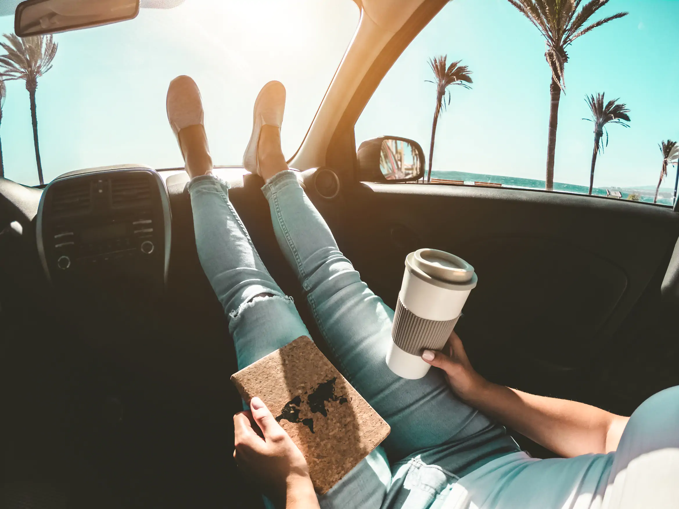 Person relaxing in car with coffee and passport by the beach.